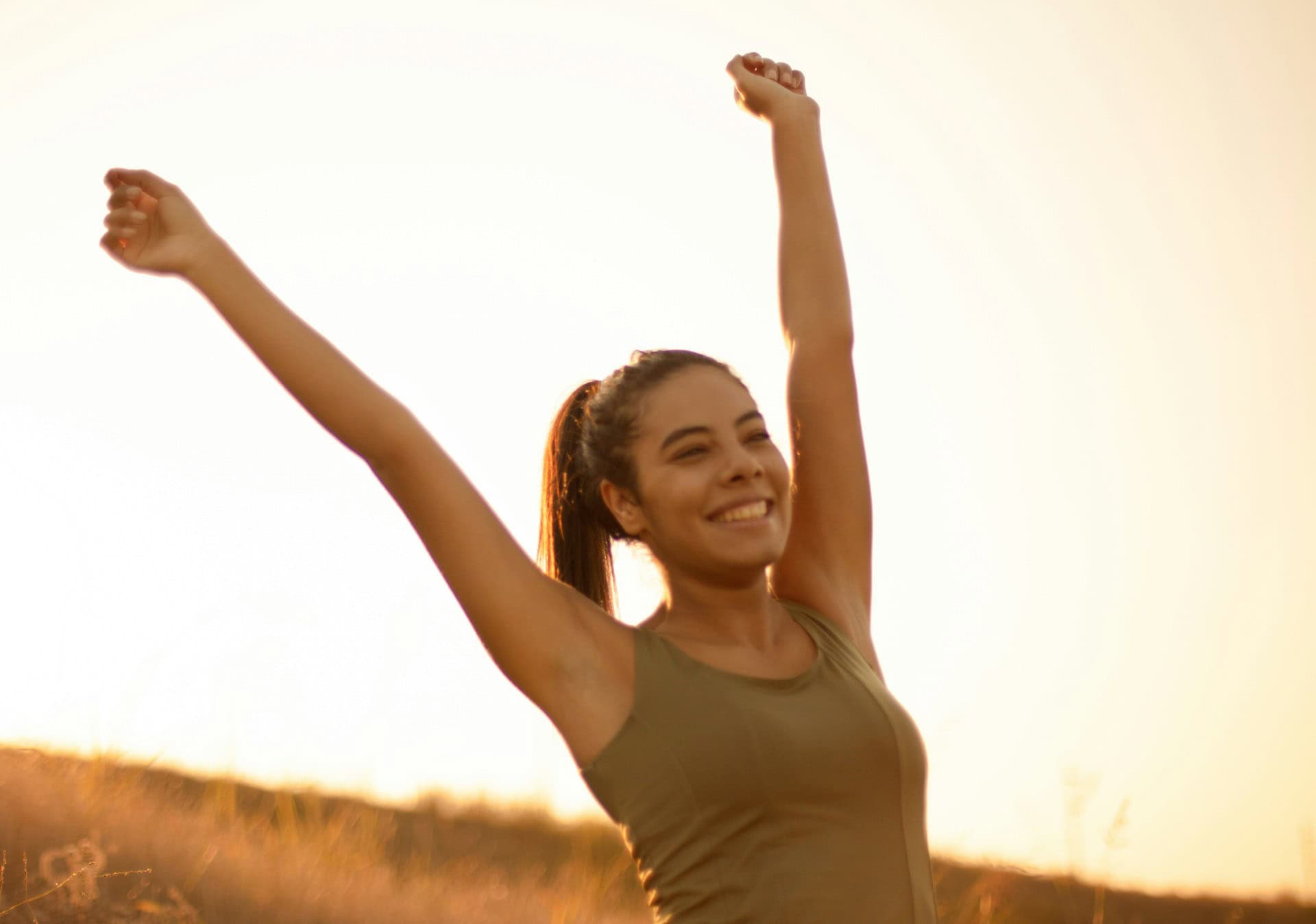 Kaitlin McMillan outdoors raising arms in sunrise.