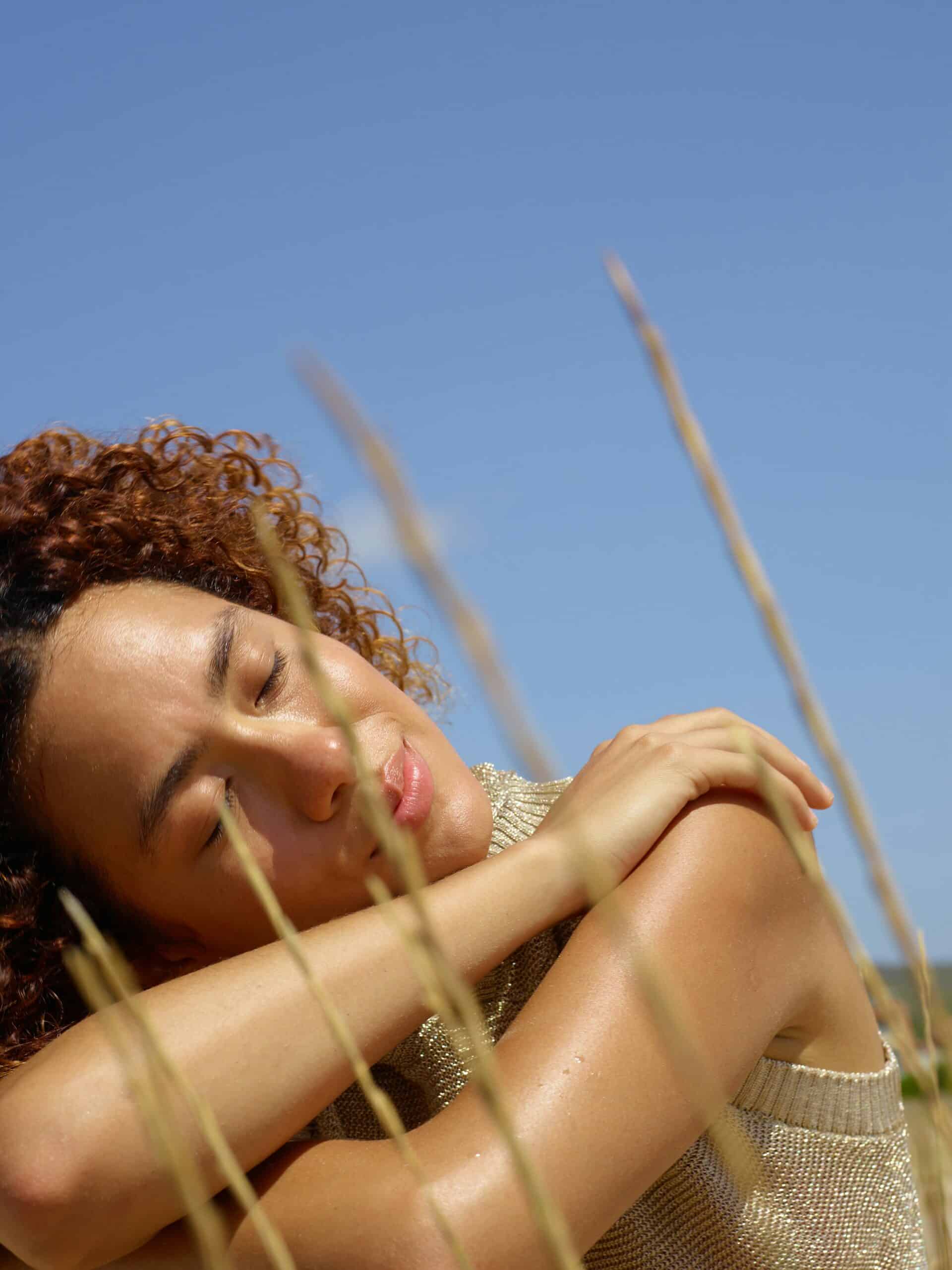 Portrait of a woman resting with arms crossed in a sunny field.